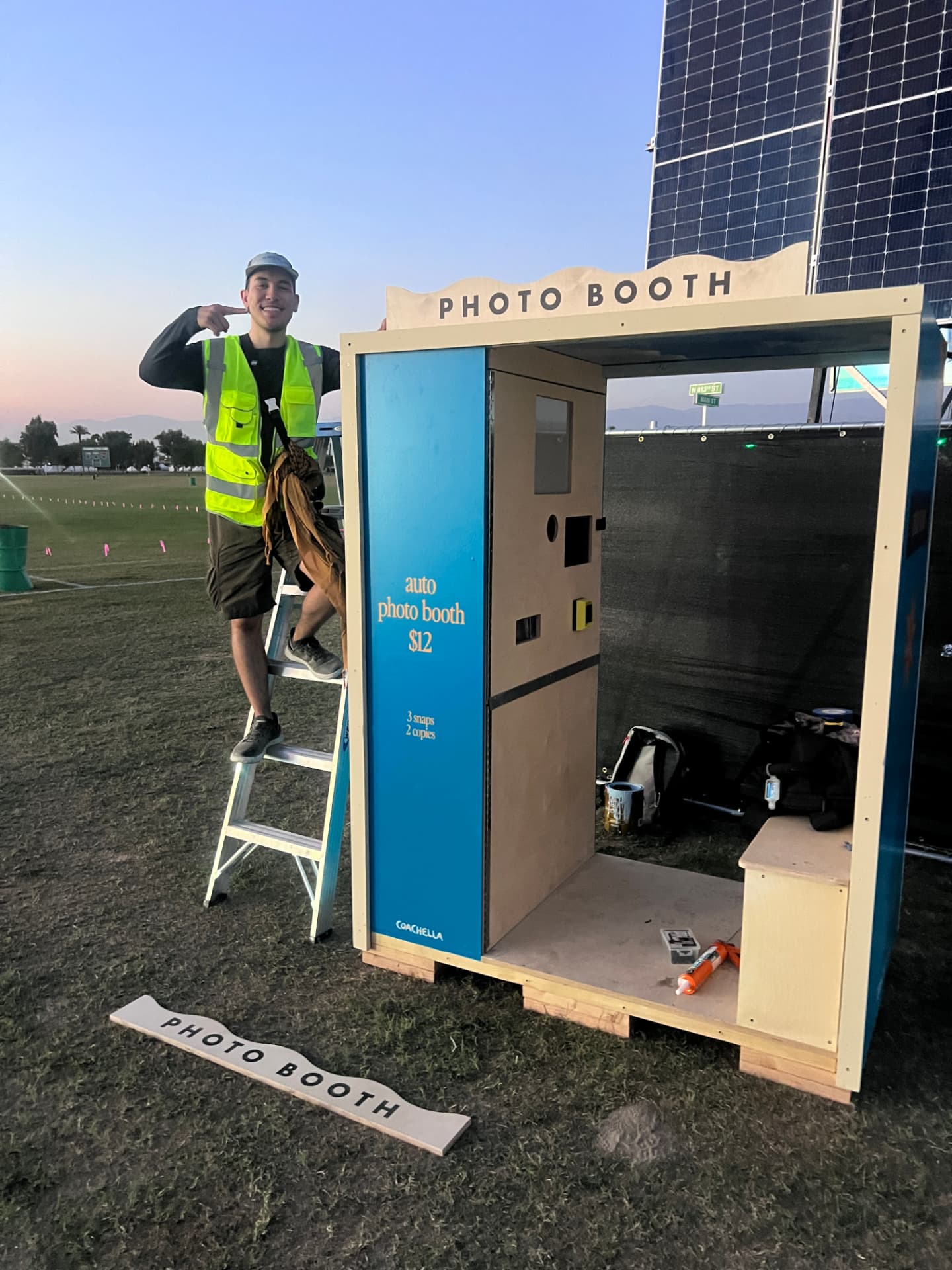 Blue auto photo booth under construction at a festival site at sunset